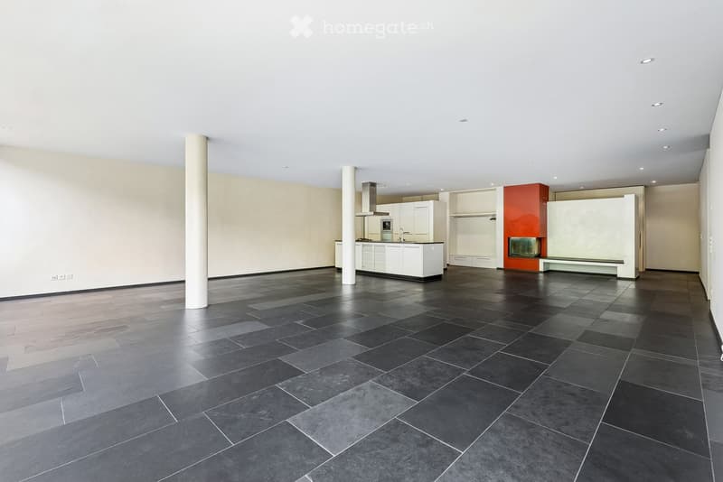 Open-plan space with a modern kitchen area featuring white cabinets, a stove, and a sink, along with a fireplace and polished dark tiles on the floor.