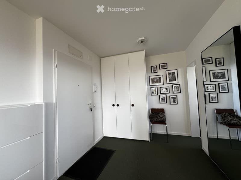 A small, furnished room with white walls, a large white wardrobe, two chairs with leopard print cushions, and several framed pictures on the wall.