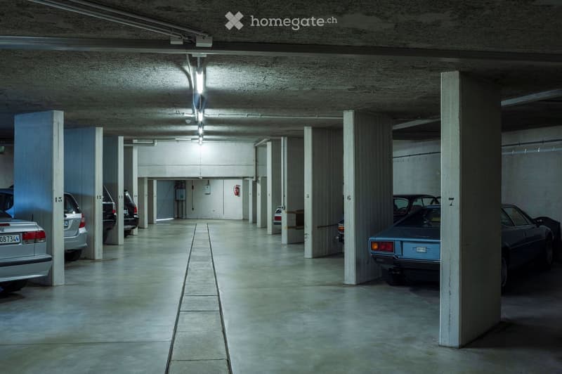 Underground parking garage with several parked cars, concrete pillars, and numbered parking spaces.