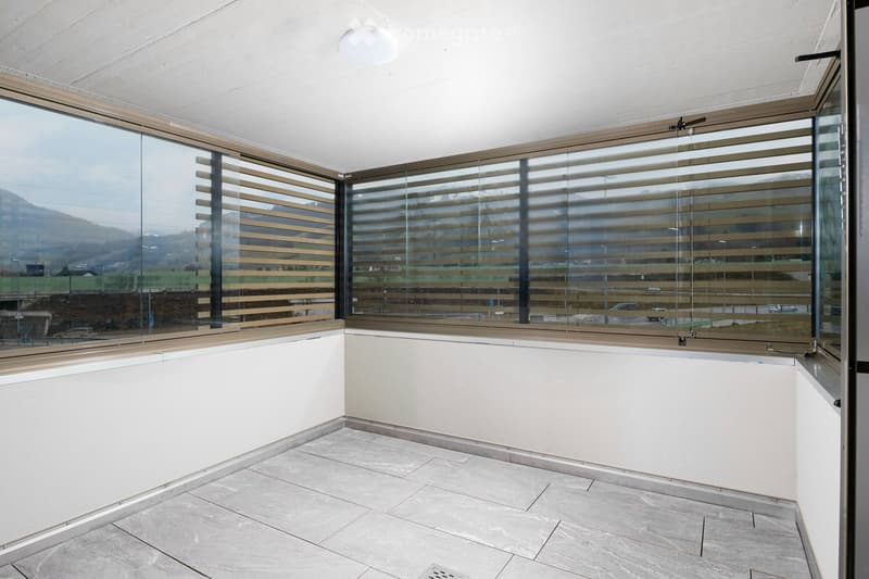empty balcony with white tiles, large windows, wooden blinds, city view