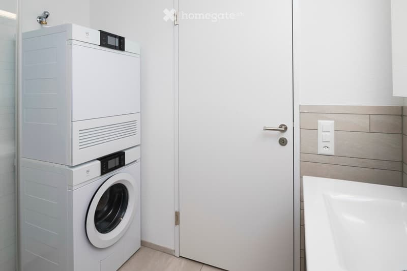 stacked washer and dryer, white wall, white door, electrical outlet, and sink