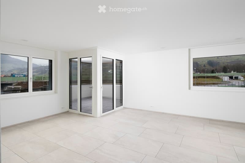 Empty room with white walls, tiled floor, large windows, and a sliding glass door leading to an outdoor area.