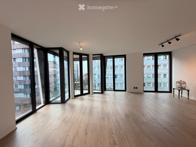 Empty room with light wooden flooring, large glass windows, and modern lighting fixtures.