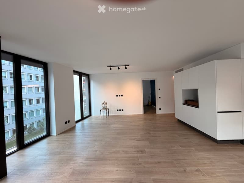 Bright, unfurnished room with wooden flooring, large windows, and a small table and chair set near the center.