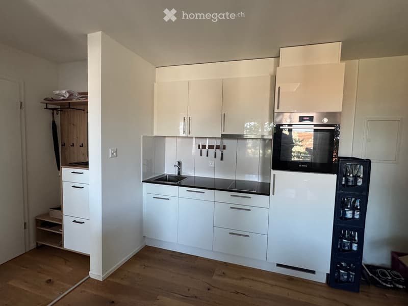 Modern kitchen with white cabinets, stainless steel appliances, and a black countertop. Includes a sink, oven, refrigerator, and a wine rack.