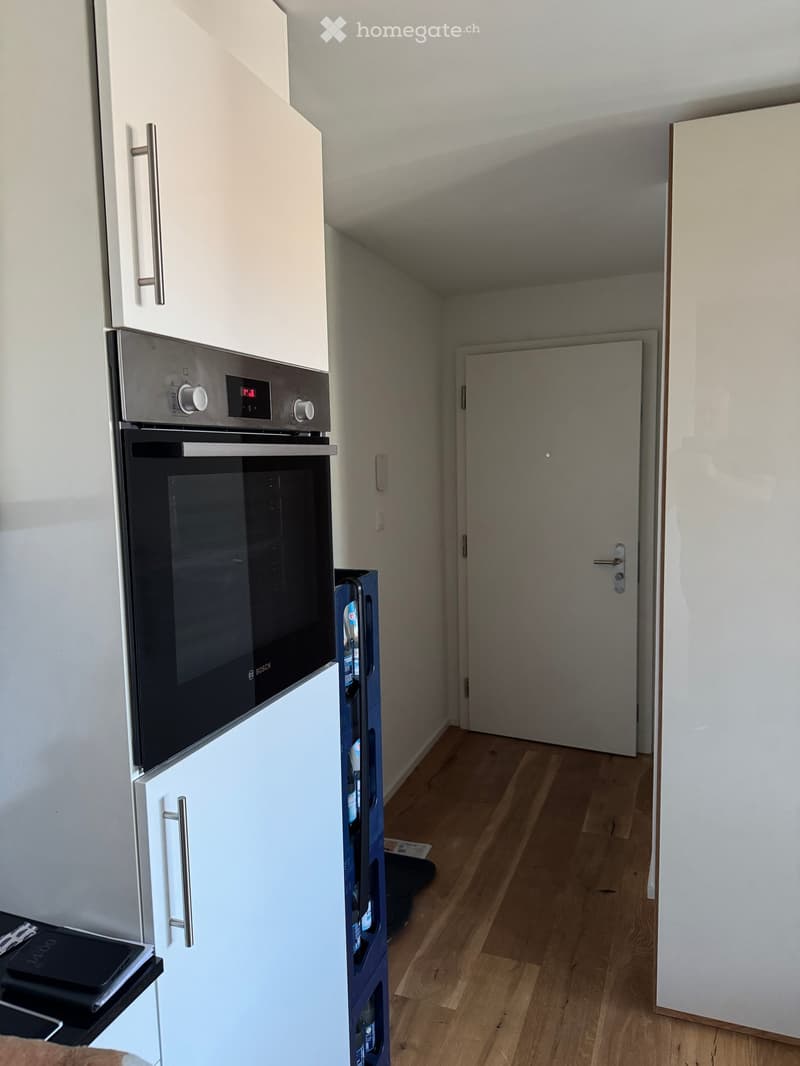 Modern kitchen with white cabinets, stainless steel oven, and wooden flooring.