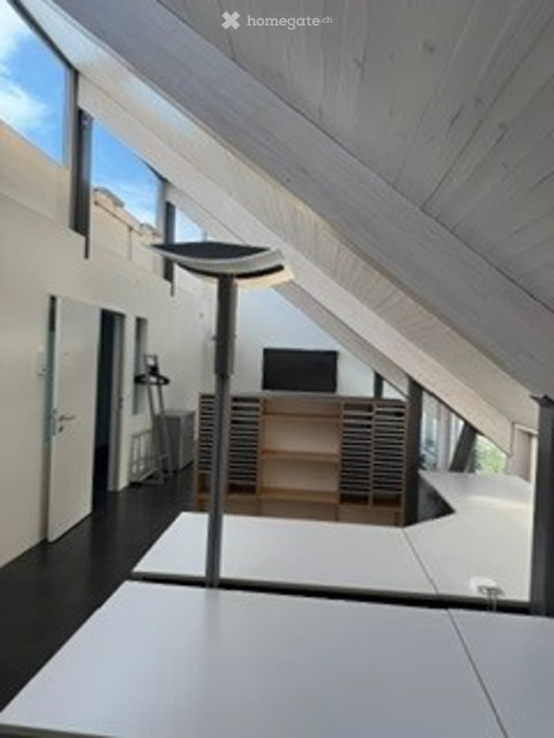 Modern, minimalist room with exposed wooden beams, large windows, a TV on a wooden stand, a tall floor lamp, and a sleek black chair.