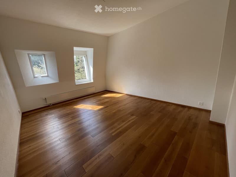 Empty room with wooden flooring and two windows allowing natural light to enter.