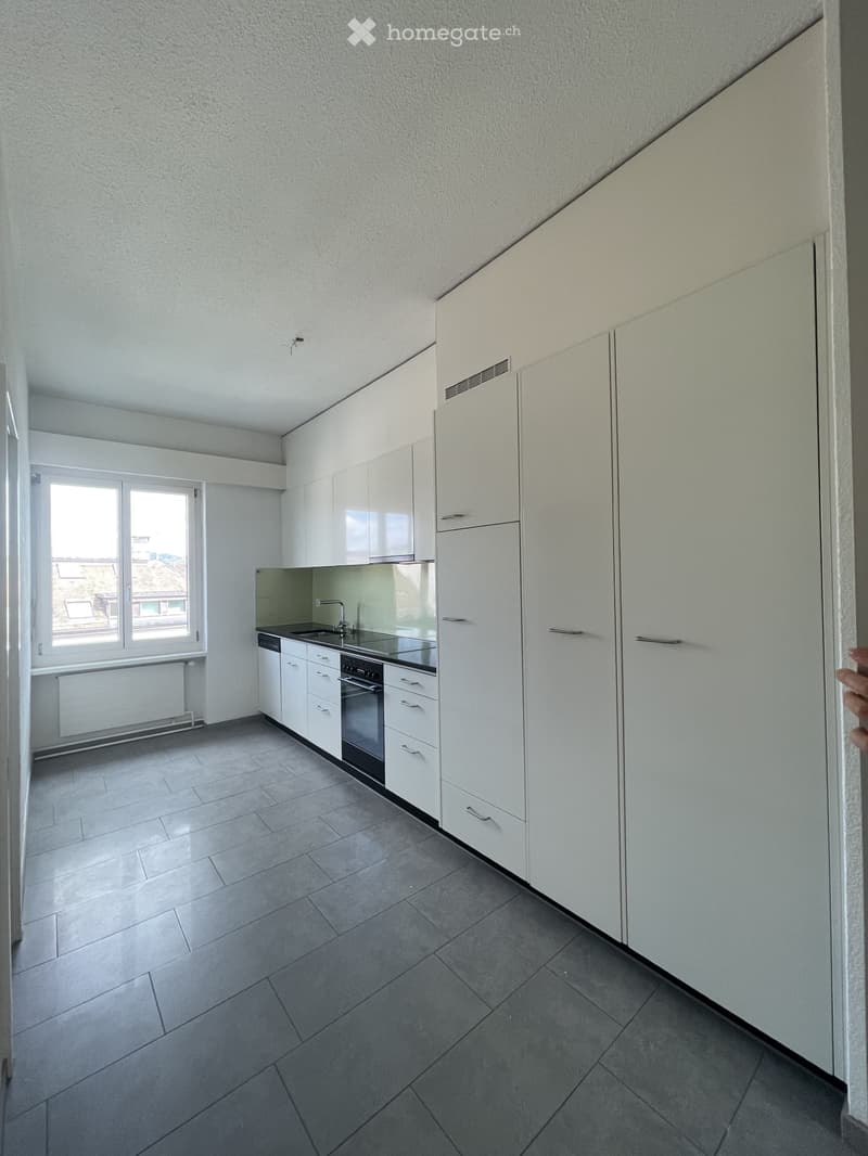 Modern kitchen with white cabinets, stainless steel sink, oven, and tiled floor. Large window provides natural light.