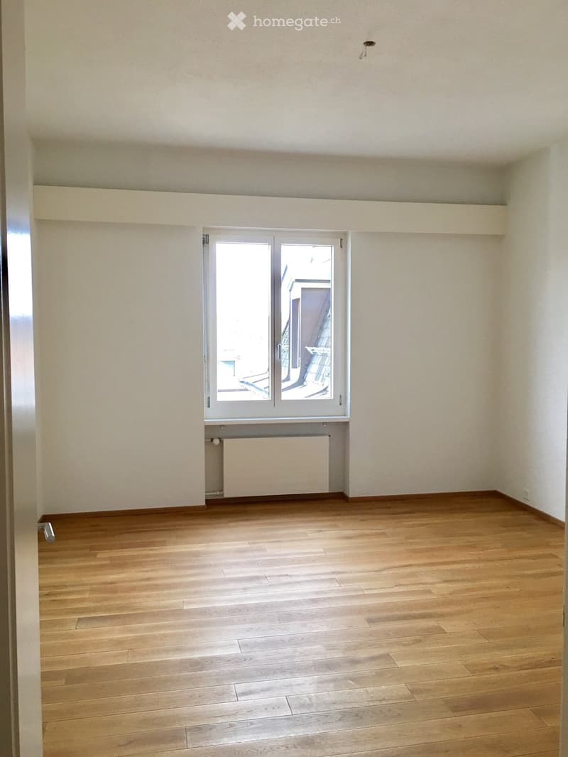 Empty room with wooden flooring, white walls, and a large window with a view of a balcony area.