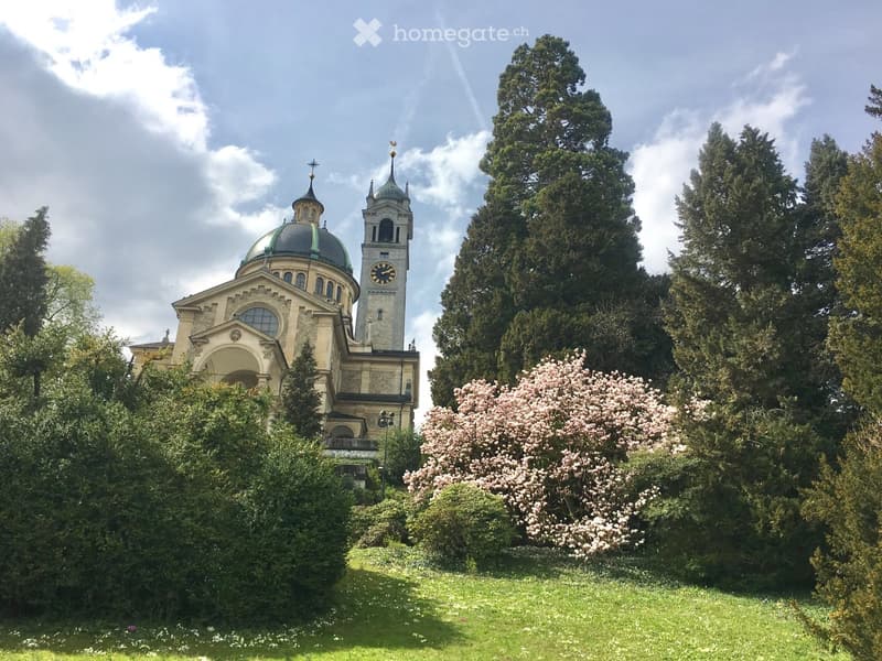 A large, ornate building with a dome and clock tower, surrounded by lush greenery and trees.
