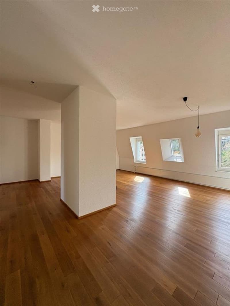 Empty room with wooden flooring, white walls, and large windows allowing natural light. No furniture or equipment present.