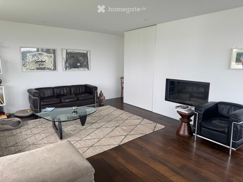 Modern living room with a black leather sofa, glass coffee table, armchair, flat-screen TV, and decorative items.