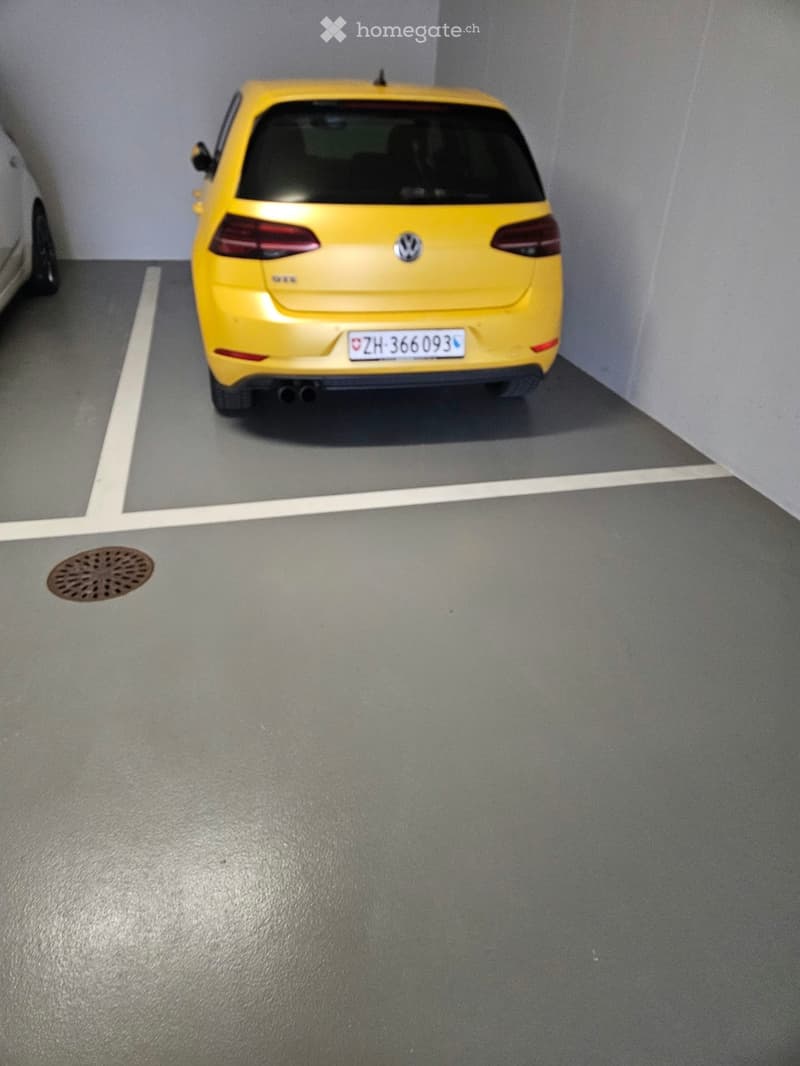 Underground parking space with a yellow Volkswagen car parked in a designated spot, gray concrete floor, and white parking lines.