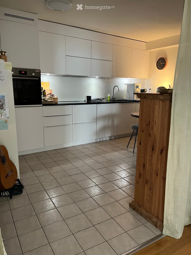 Modern kitchen with white cabinets, stainless steel appliances, tiled floor, bar counter, and a guitar leaning against the wall.