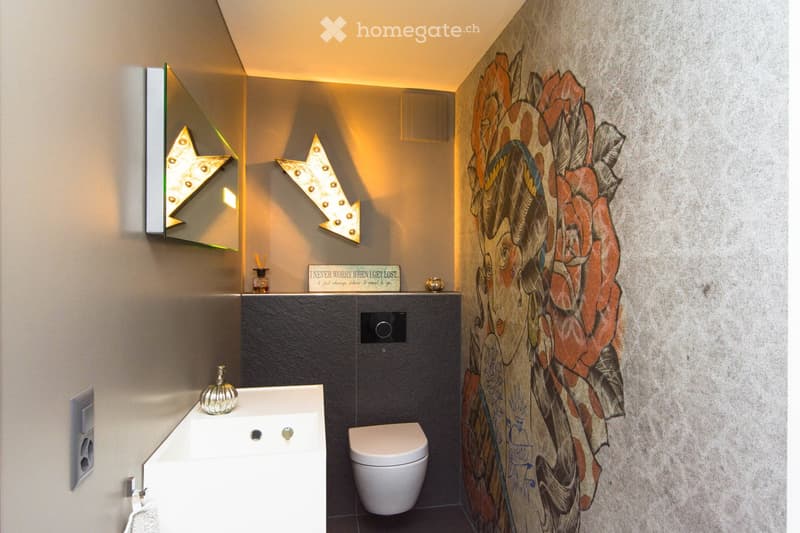 Modern bathroom with a white sink, toilet, decorative wall art, and stylish lighting fixtures.