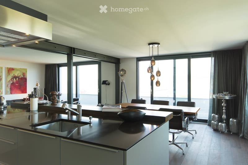 Modern kitchen with sleek black countertops, stainless steel sink, and pendant lights. Features a dining area with a table and chairs, a globe lamp, and artwork on the wall.