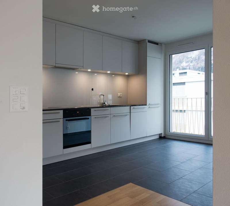 Modern kitchen with grey cabinets, black tiled floor, and a large window with a balcony view.