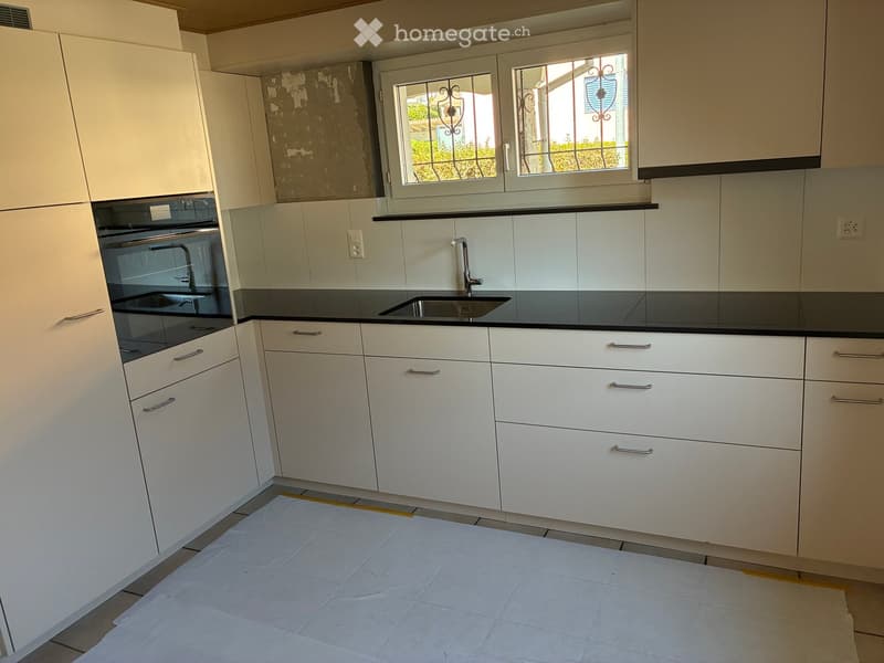 Modern kitchen with white cabinets, black countertops, a sink with a modern faucet, and an oven. The floor is covered with protective plastic sheeting.