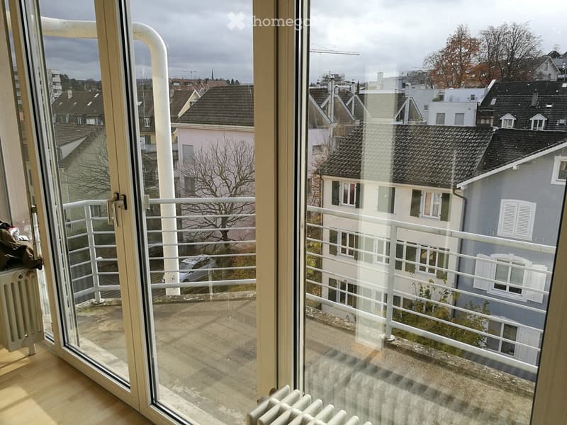 Balcony with white metal railing, overlooking a cityscape with residential buildings and trees.