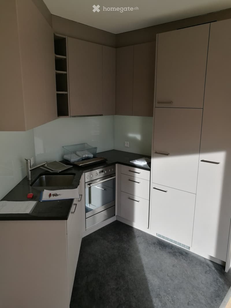 Modern kitchen with white cabinets, black countertops, and stainless steel appliances including a sink, faucet, and oven. The floor is dark grey tile.