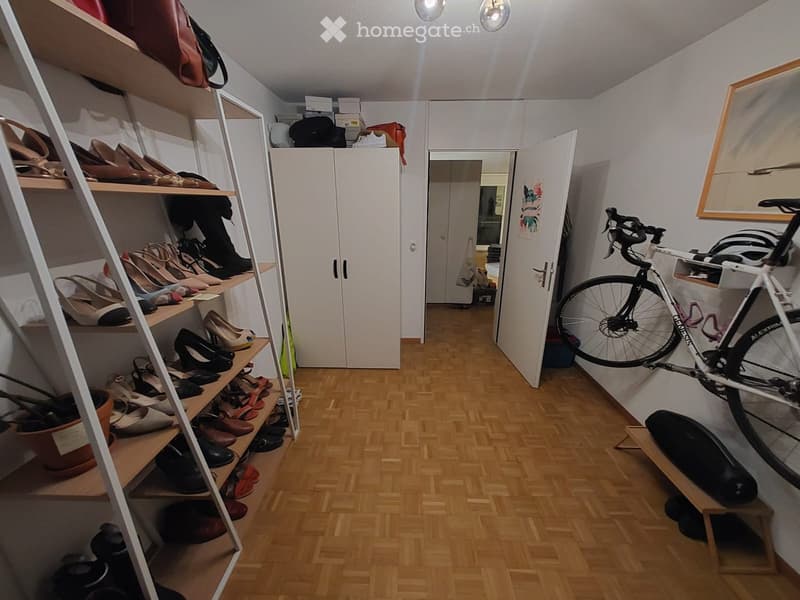 A hallway with wooden floors, a white cabinet, a bicycle mounted on the wall, and a shoe rack with various shoes.