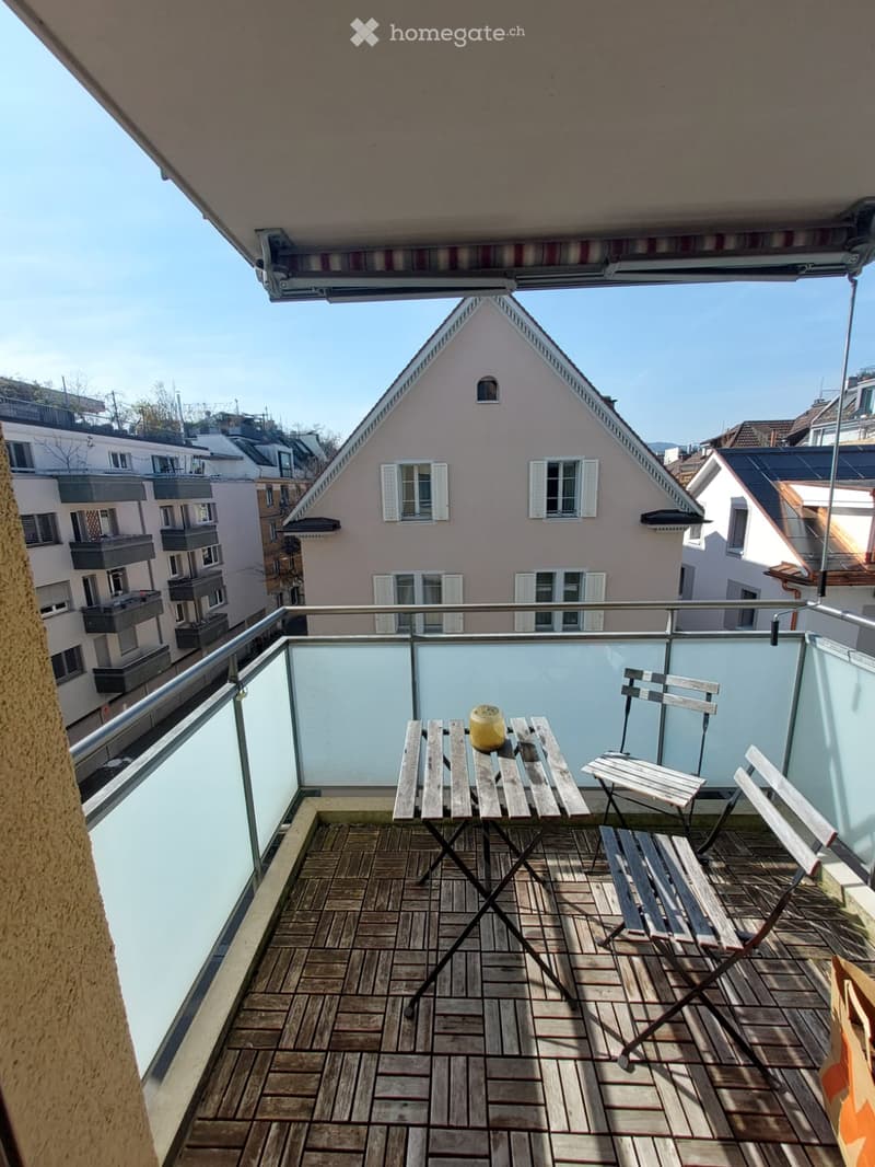 Balcony with wooden floor, metal railing, table, chairs, and a view of the city