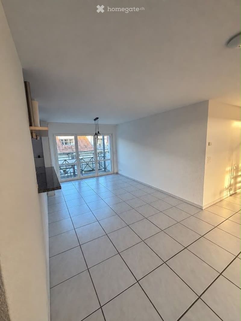 Empty room with white tiled flooring, white walls, and a large sliding glass door leading to a balcony or terrace area.