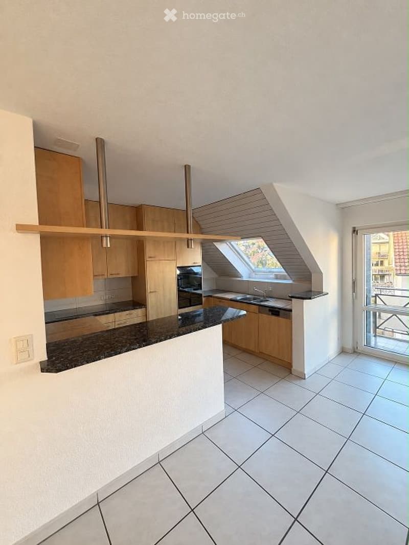 Modern kitchen with light wooden cabinets, granite countertop, and a window overlooking a balcony.