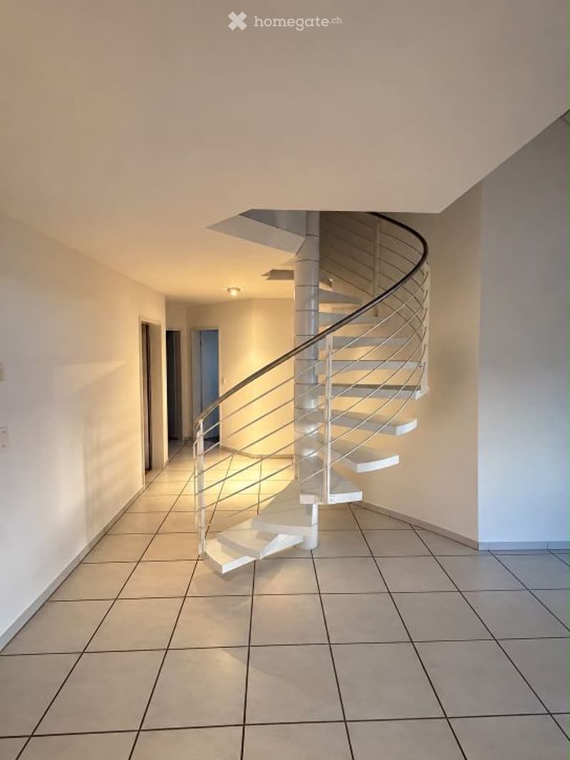 Modern hallway with a sleek, white spiral staircase featuring a metal railing, beige tiled flooring, and soft ambient lighting.