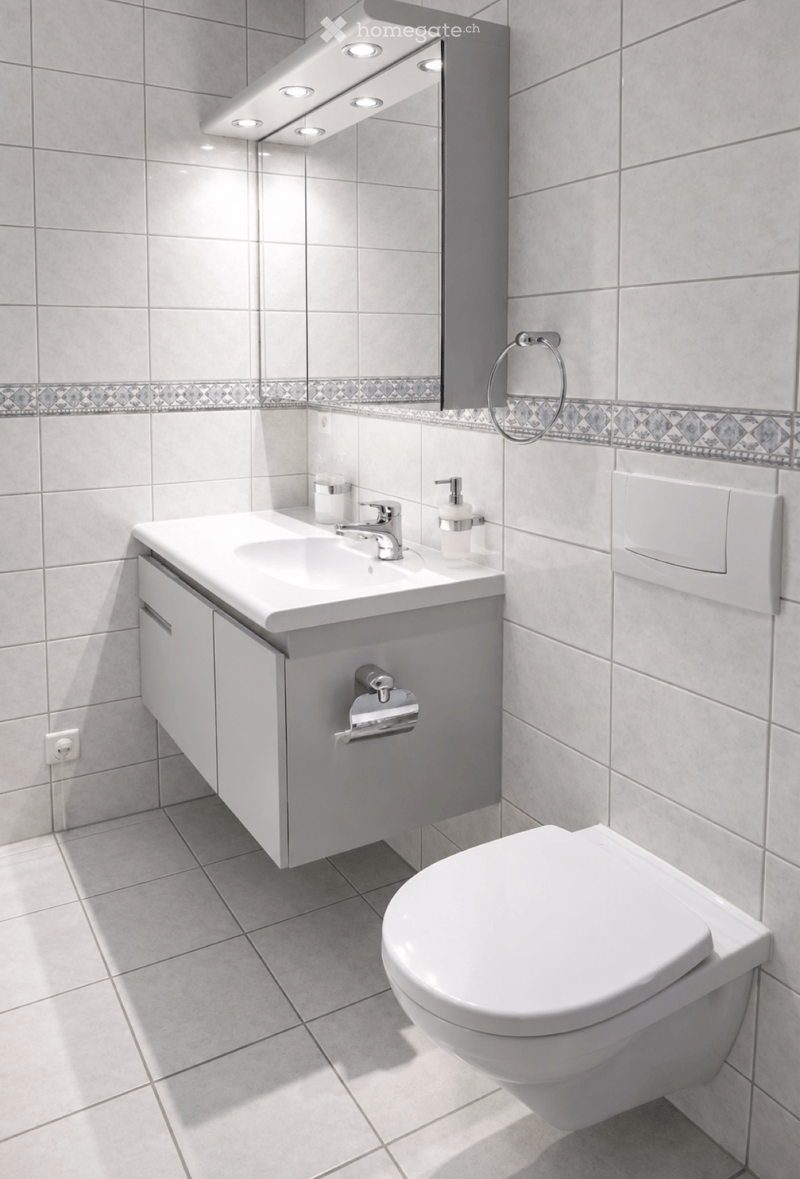 Modern bathroom with white tiles, a white sink with a modern faucet, a toilet, a large mirror with built-in lighting, and a towel ring.