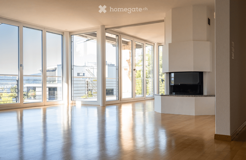 Empty living space with polished wooden floor, large glass doors leading to a balcony, and a modern fireplace.