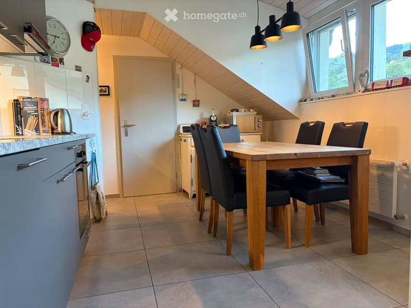 Bright kitchen with a dining area, featuring a wooden dining table with four black chairs, a refrigerator, oven, microwave, and various kitchen items on the counter.