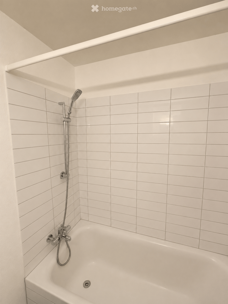 Modern bathroom with white tiled walls and a bathtub, featuring a handheld showerhead and a sleek faucet.