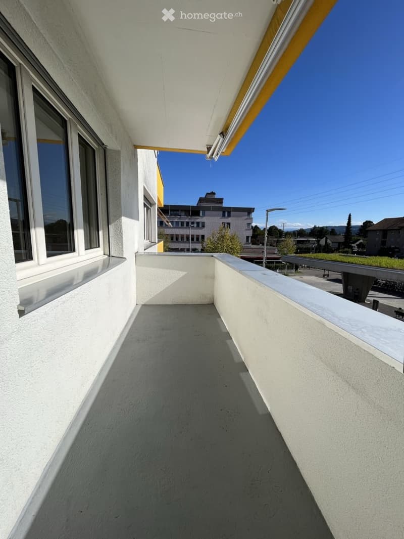Balcony with white walls, large windows, and a clear view of the surrounding area.