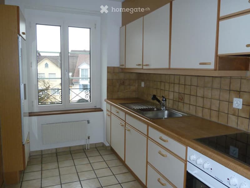 Bright kitchen with white cabinets, wooden countertops, tiled floor, and a window overlooking the street.