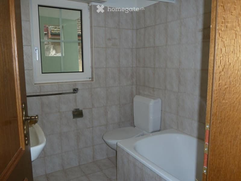 A small bathroom with a toilet, bathtub, sink, and a window with a view of another room.