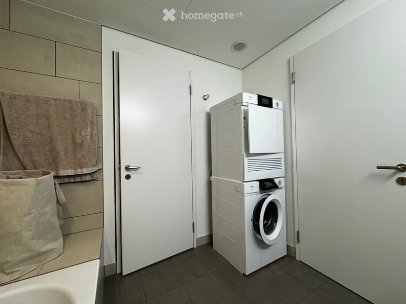 Modern bathroom with a stacked washing machine and dryer, a towel hanging on a rack, and a laundry basket on the floor.