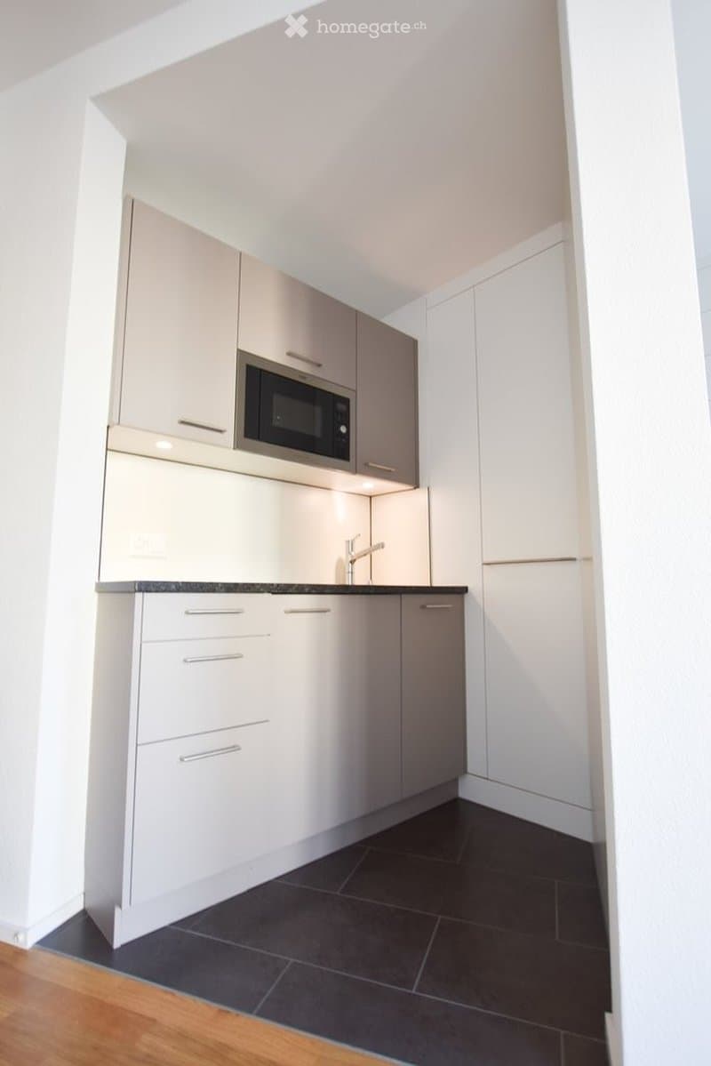 Modern kitchen with white cabinets, a microwave, and a black countertop. The floor is dark tiled, and the walls are white.