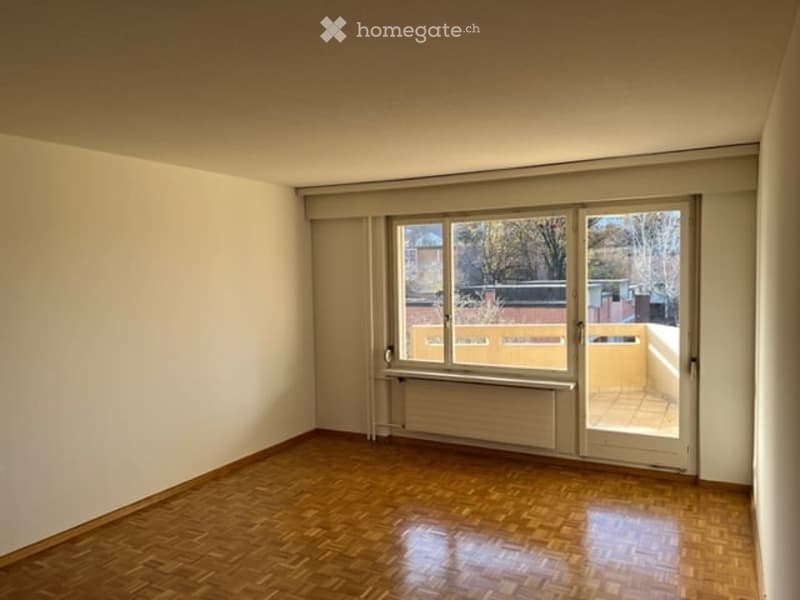 Empty room with wooden flooring, large window, and sliding glass door leading to a balcony.
