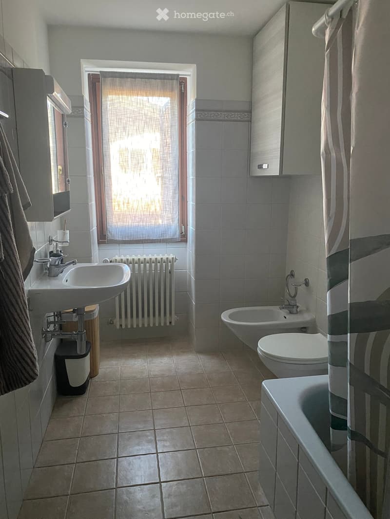 Bathroom with a sink, toilet, bathtub, and radiator. Features tiled walls and floor, a window with blinds, and a cabinet above the sink.