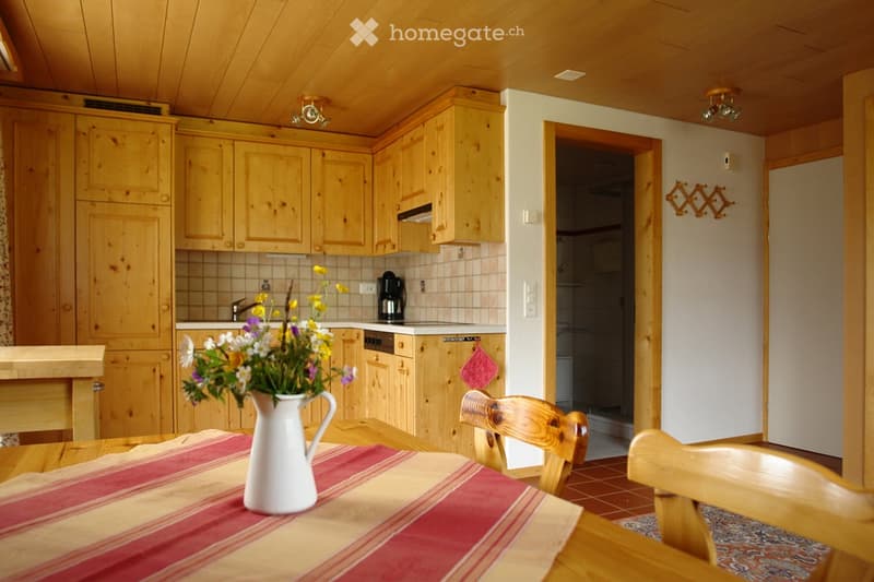 Cozy kitchen with wooden cabinets, a dining table with chairs, a vase of flowers, and a coffee maker on the counter.