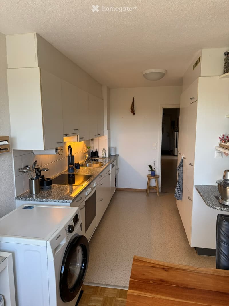 Modern kitchen with white cabinets, granite countertops, stainless steel appliances, and a small wooden stool near the doorway.