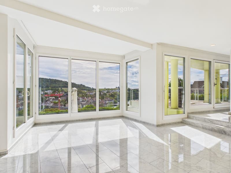 Bright, empty room with large windows and a marble floor, offering a scenic view of the city and surrounding landscape.