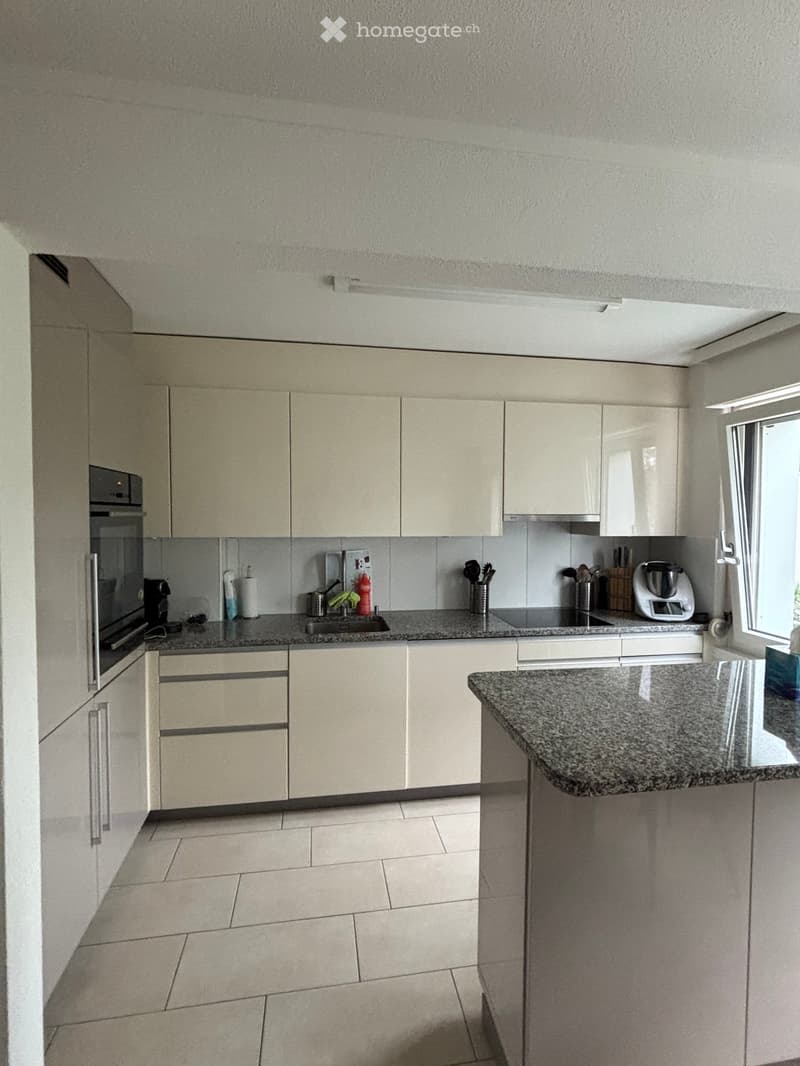 Modern kitchen with light-colored cabinets, granite countertop, and various appliances including an oven, sink, and blender.