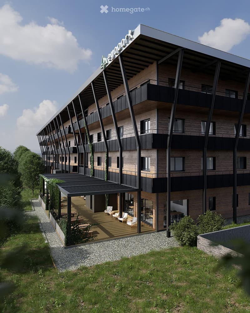 Modern multi-story building with wooden and glass facade, balconies, and a covered outdoor seating area with chairs and tables.