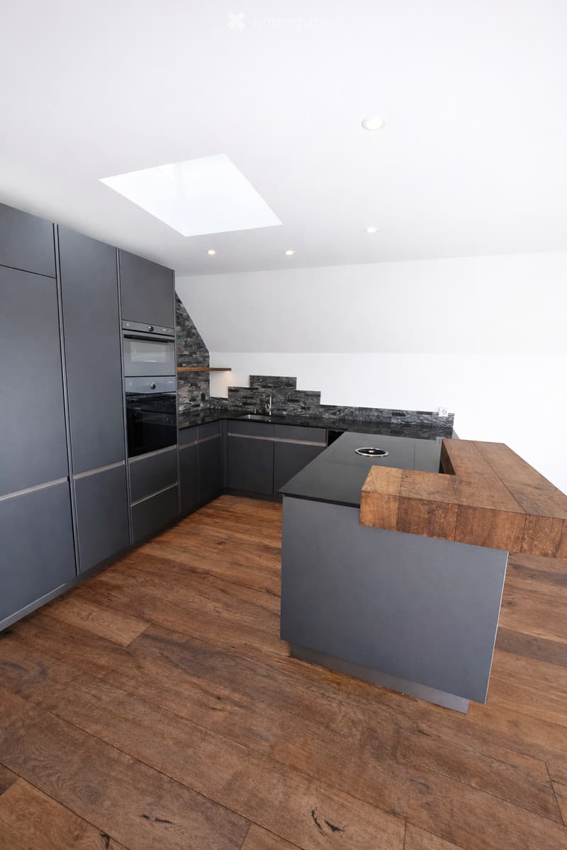Modern kitchen with grey cabinets, wooden floor, central island, and built-in appliances.