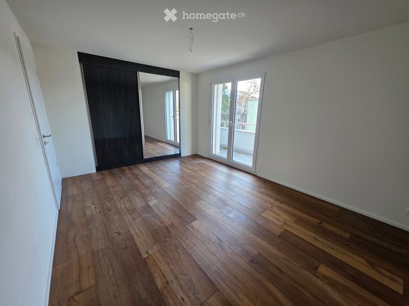 Empty room with wooden flooring, white walls, large sliding glass doors leading to a balcony, and a mirrored closet.