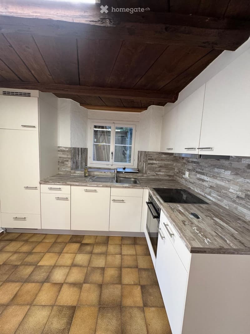 Modern kitchen with white cabinets, wooden countertop, tiled floor, and stainless steel sink and oven.
