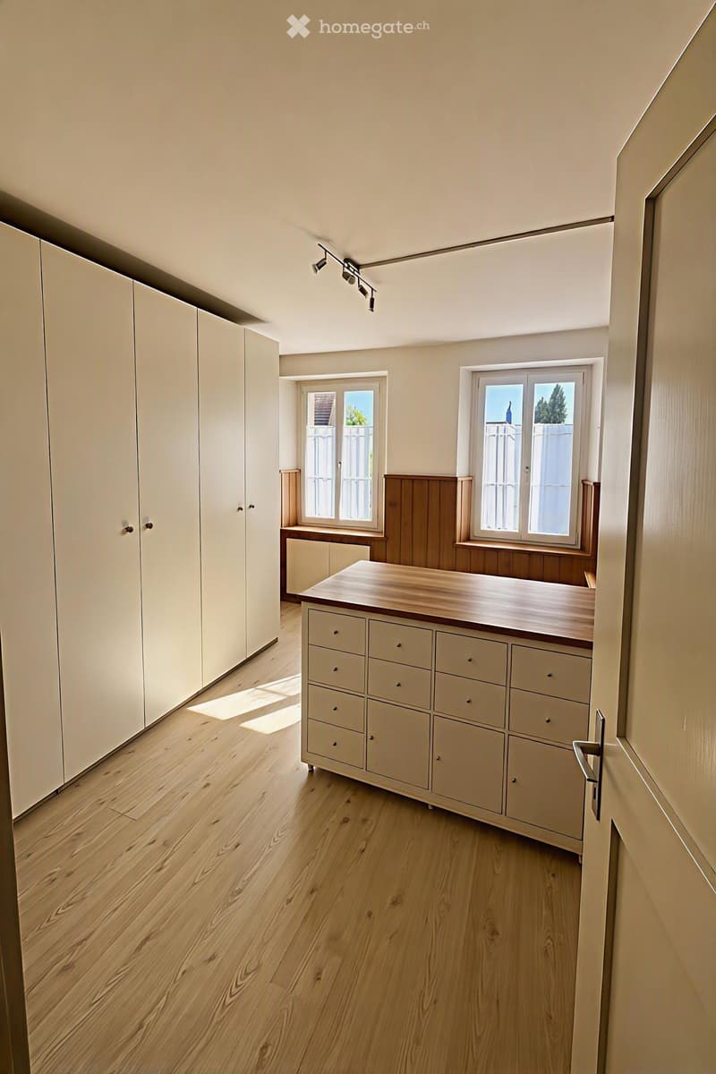Bright, minimalist kitchen with light wooden flooring, white cabinets, and a central kitchen island with drawers.